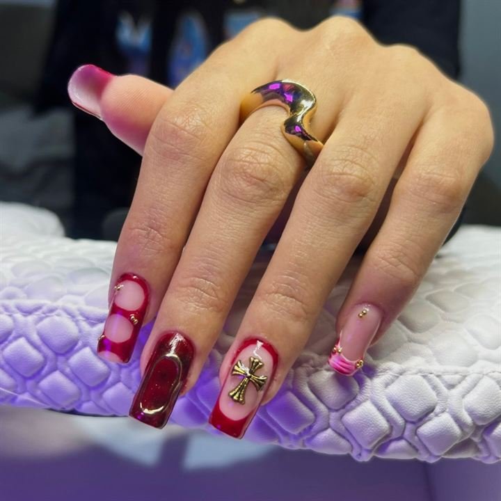 Nail art em vermelho com cruz dourada, corações e pedrarias